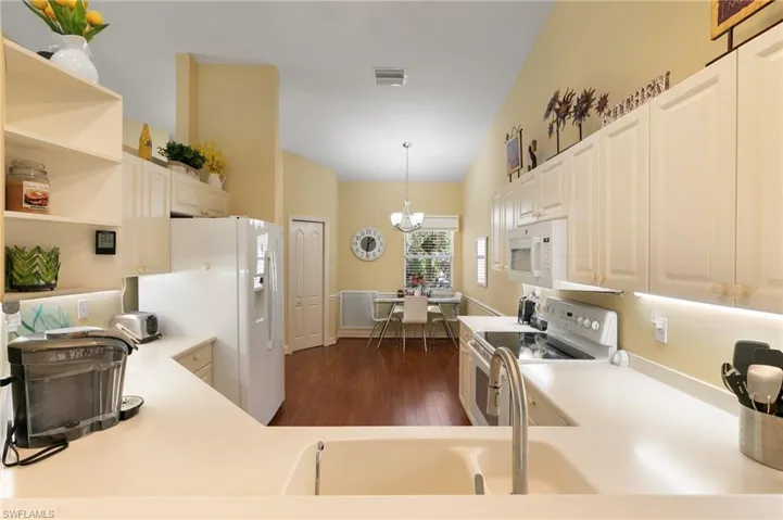 Kitchen with white appliances, dark wood-style floors, open shelves, light countertops, and vaulted ceiling
