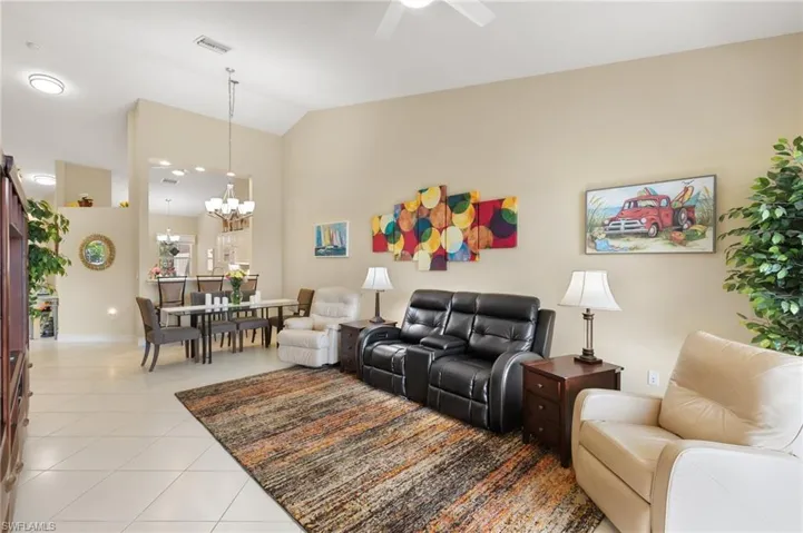 Living area featuring light tile patterned flooring, lofted ceiling, hanging lights, and ceiling fan