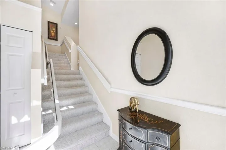 (Virtual wall color change) Entryway from front door showing carpeted stairs, coat closet, and chair lift.