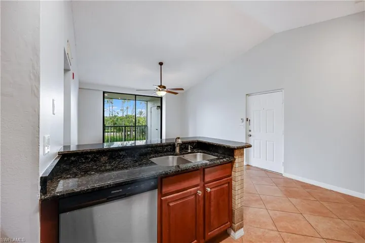 Kitchen featuring sink, lofted ceiling, dark stone countertops, dishwasher, and ceiling fan