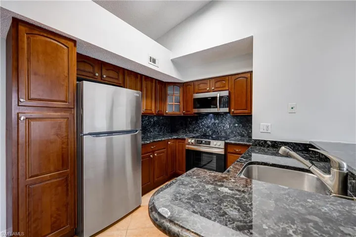 Kitchen with stainless steel appliances, vaulted ceiling, sink, light tile patterned floors, and decorative backsplash