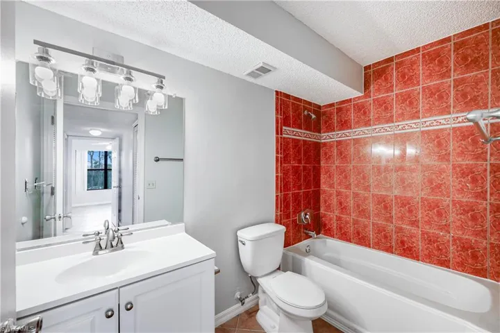 Full bathroom with vanity, tile patterned floors, tiled shower / bath combo, toilet, and a textured ceiling