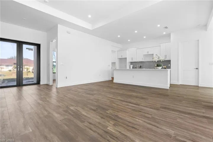 Expansive open-concept living space featuring wood-finish flooring, a tray ceiling with recessed lighting, and a modern kitchen with white cabinetry