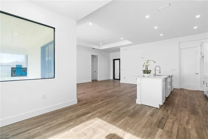 Spacious open concept interior featuring wood-finish flooring, recessed lighting, a kitchen island with an undermount sink, and white cabinetry