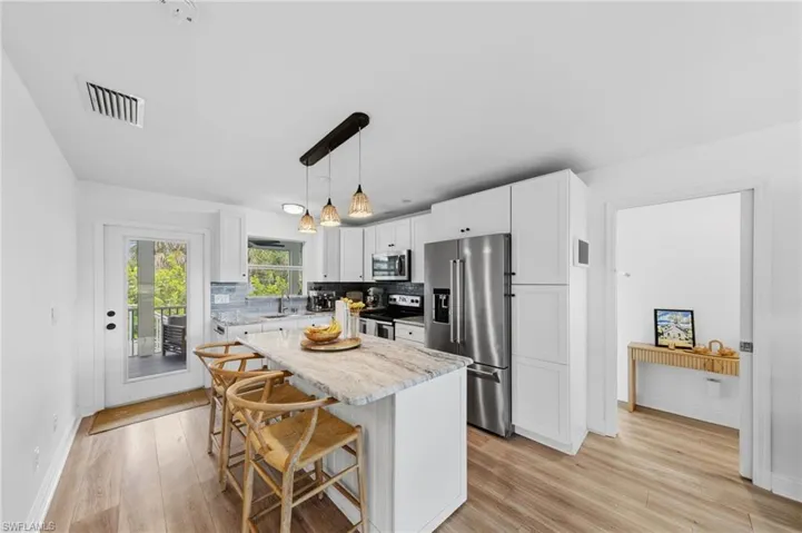 Kitchen featuring a breakfast bar, stainless steel appliances, light wood finished floors, and light stone countertops