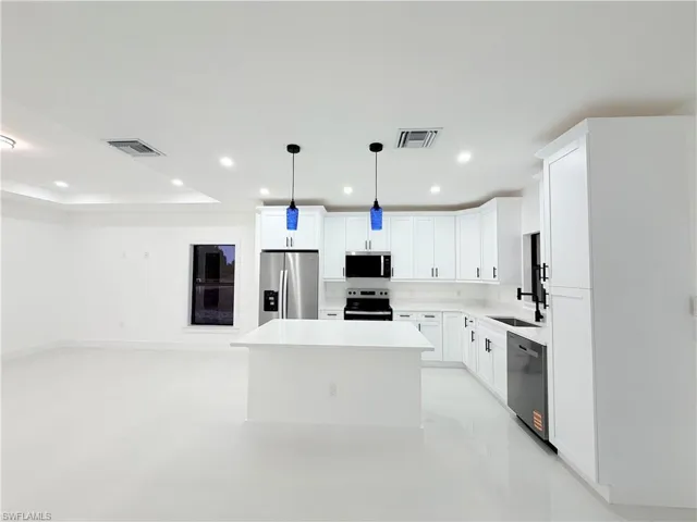 Kitchen featuring white cabinets, a center island, hanging light fixtures, open floor plan, and stainless steel appliances