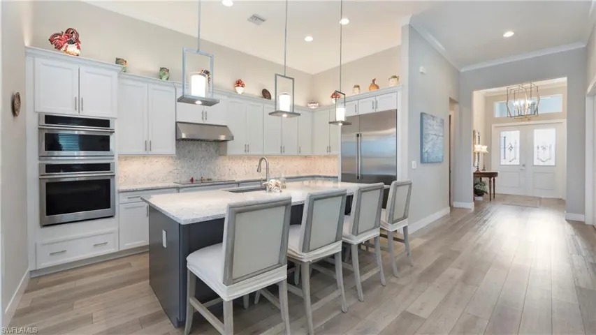 Kitchen with hanging light fixtures, decorative backsplash, ornamental molding, stainless steel double oven, and a kitchen island with sink