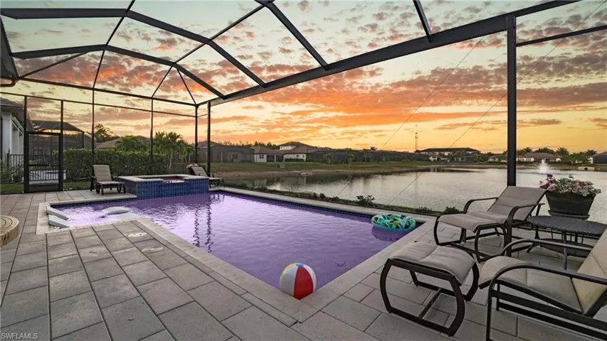 Pool at dusk featuring a water view, a sunroom, a pool with connected hot tub, a lanai, and a patio