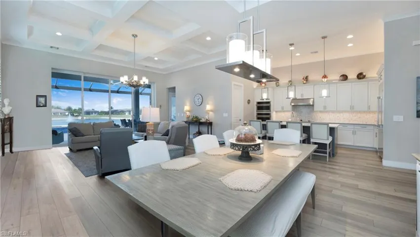Dining area with a water view, a towering ceiling, coffered ceiling, beamed ceiling, and light wood finished floors
