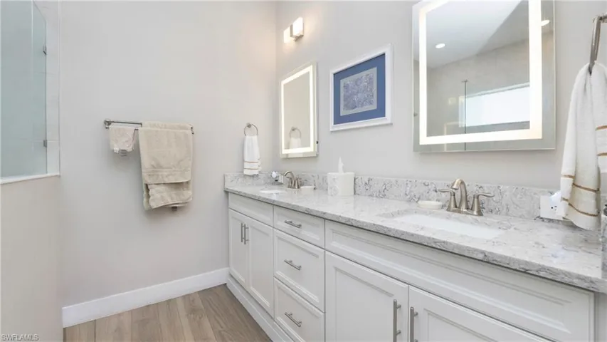 Bathroom featuring double vanity, light wood-style floors, and a tile shower