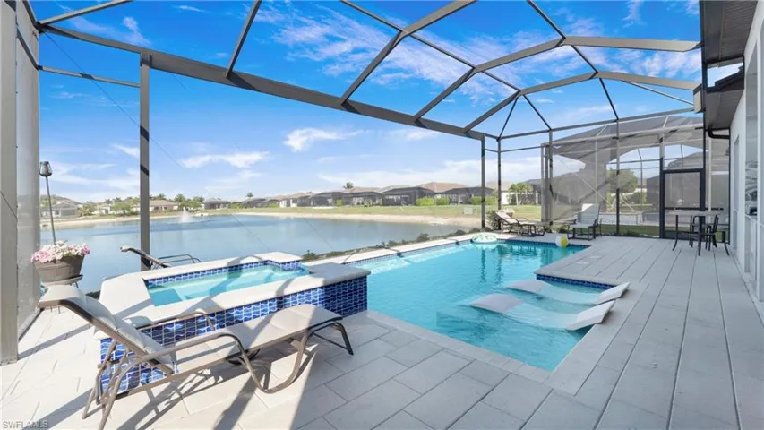 View of pool featuring glass enclosure, a sunroom, a patio area, a water view, and a pool with connected hot tub