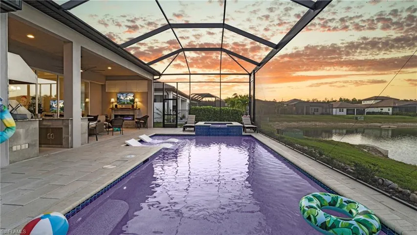 View of swimming pool featuring a sunroom, exterior kitchen, a patio area, glass enclosure, and a pool with connected hot tub