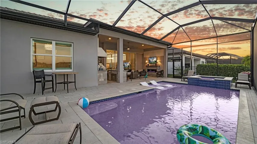 View of pool featuring a sunroom, glass enclosure, a patio area, an outdoor kitchen, and a pool with connected hot tub