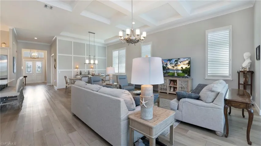 Living area with a chandelier, ornamental molding, light wood-type flooring, coffered ceiling, and beam ceiling