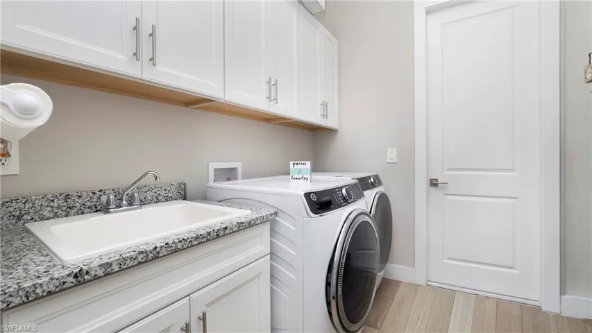 Laundry room with washer and clothes dryer, cabinet space, and light wood-style flooring