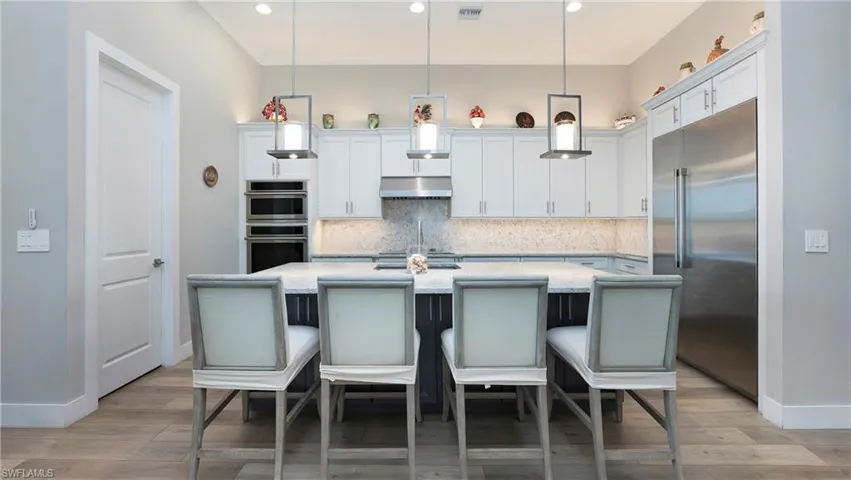 Kitchen with stainless steel appliances, white cabinets, decorative light fixtures, a center island with sink, and tasteful backsplash