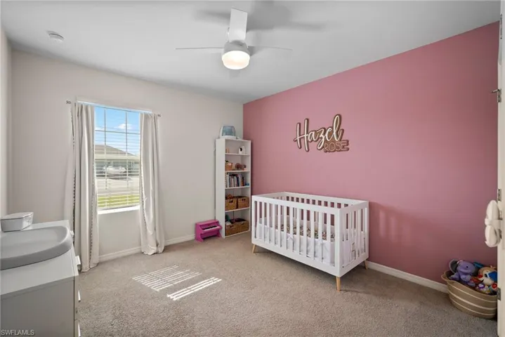 Carpeted bedroom featuring sink, a nursery area, and ceiling fan