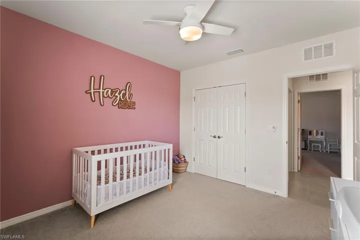 Carpeted bedroom featuring ceiling fan, a nursery area, and a closet