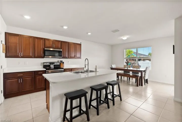 Kitchen with a center island with sink, a kitchen breakfast bar, sink, light tile patterned flooring, and stainless steel appliances