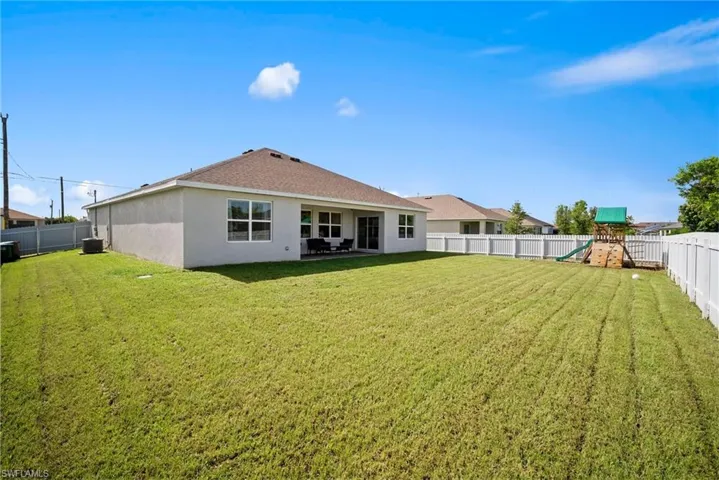 Rear view of property featuring central AC unit, a playground, and a yard