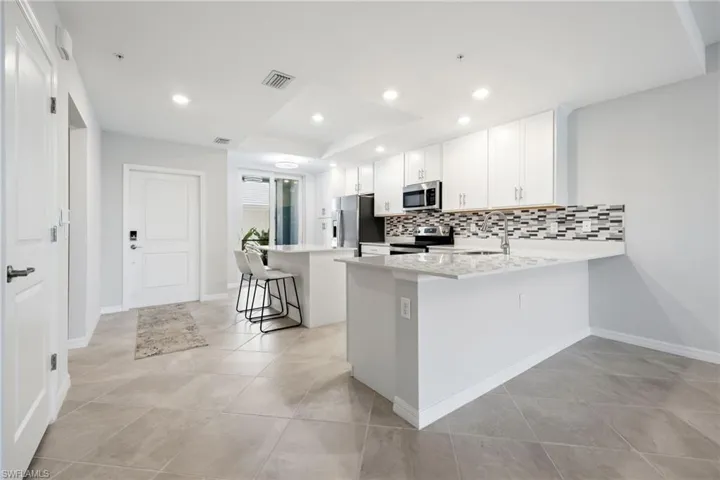 Kitchen featuring a kitchen breakfast bar, white cabinets, decorative backsplash, a peninsula, and stainless steel appliances