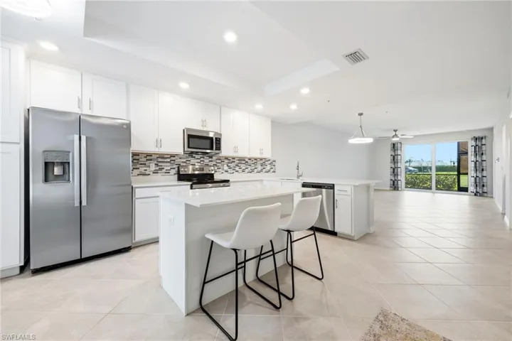 Open kitchen with white cabinetry, stainless steel appliances, tile backsplash, island and breakfast bar