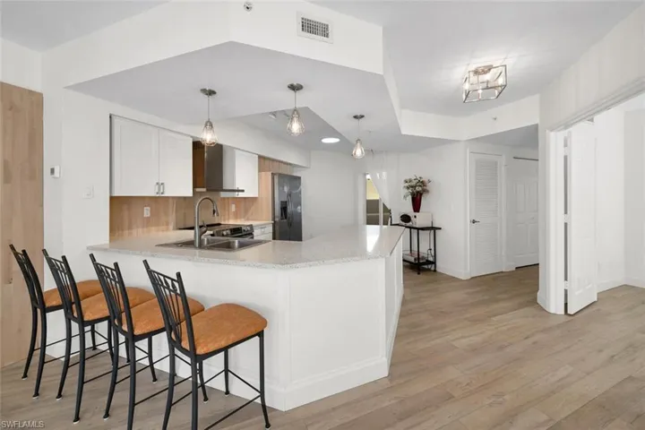 Kitchen featuring white cabinets, sink, light hardwood / wood-style flooring, stainless steel fridge, and kitchen peninsula