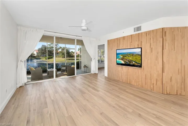 Unfurnished living room featuring hardwood / wood-style floors, a water view, ceiling fan, and wooden walls