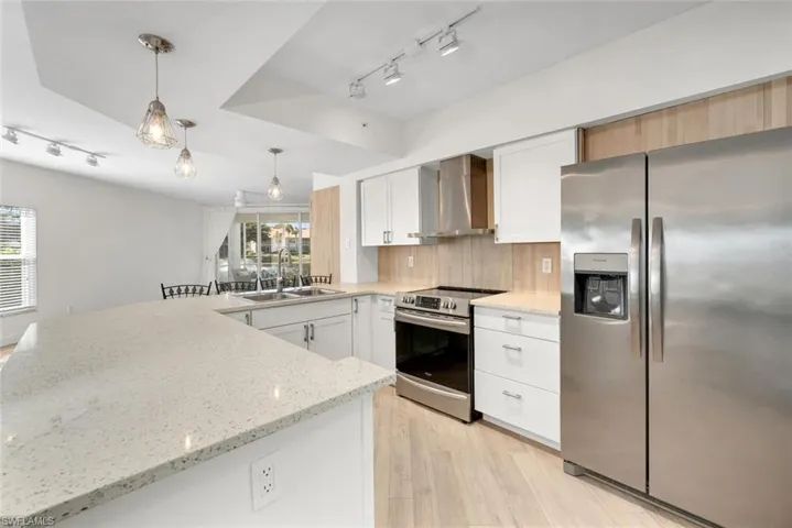 Kitchen with white cabinetry, stainless steel appliances, wall chimney range hood, pendant lighting, and light wood-type flooring