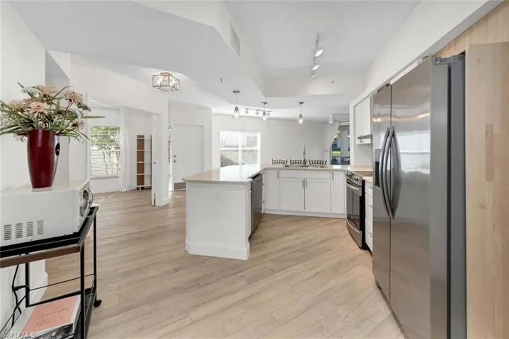 Kitchen featuring kitchen peninsula, light wood-type flooring, a wealth of natural light, stainless steel appliances, and white cabinets