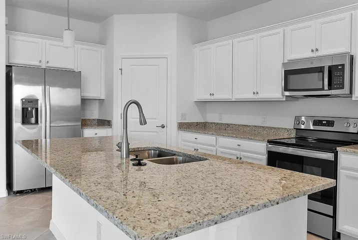 Kitchen featuring an island with a double basin sink, stainless steel appliances, white cabinetry, and granite countertops