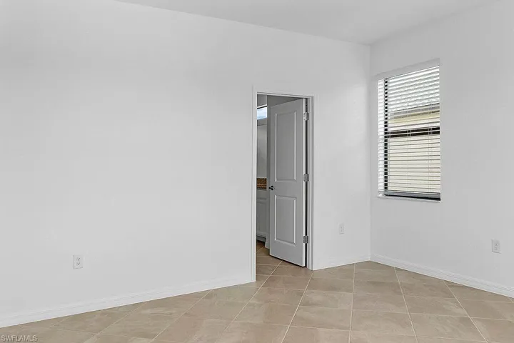 Neutral tile flooring, white walls, and a window with blinds