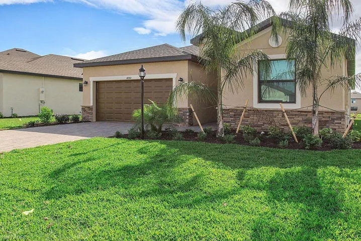 Stucco exterior with a stone veneer accent, attached garage, paver driveway, and front landscaping