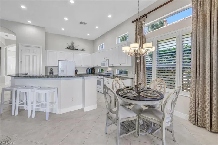 Kitchen featuring white appliances, white cabinetry, light tile patterned floors, and dark stone counters