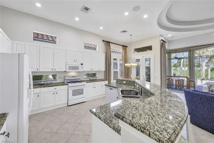 Kitchen featuring white cabinetry, light tile patterned floors, a center island with sink, and white appliances