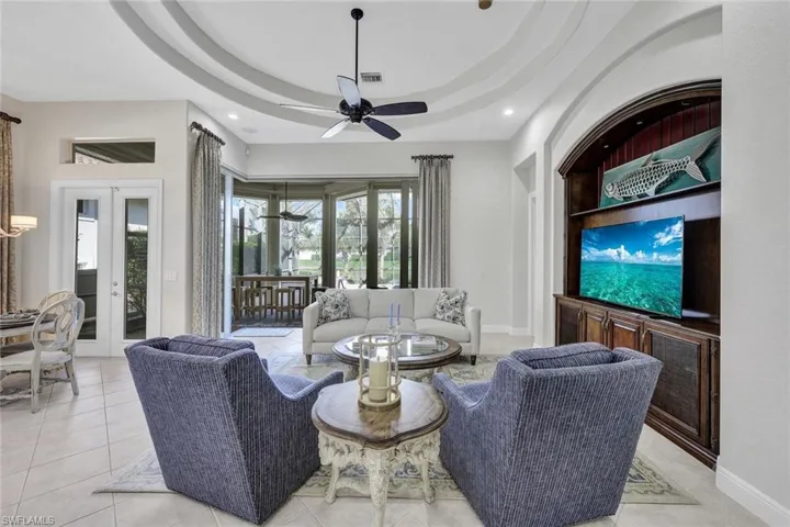 Tiled living room featuring ceiling fan, a raised ceiling, and french doors