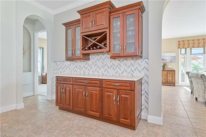Custom Built-in Bar with decorative backsplash, crown molding, and light tile patterned flooring