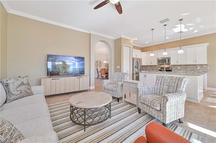 Living room with ceiling fan, crown molding, and light tile patterned flooring