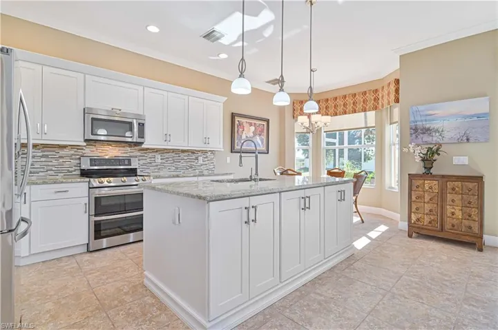 Kitchen with a kitchen island with sink, white cabinets, hanging light fixtures, sink, and appliances with stainless steel finishes