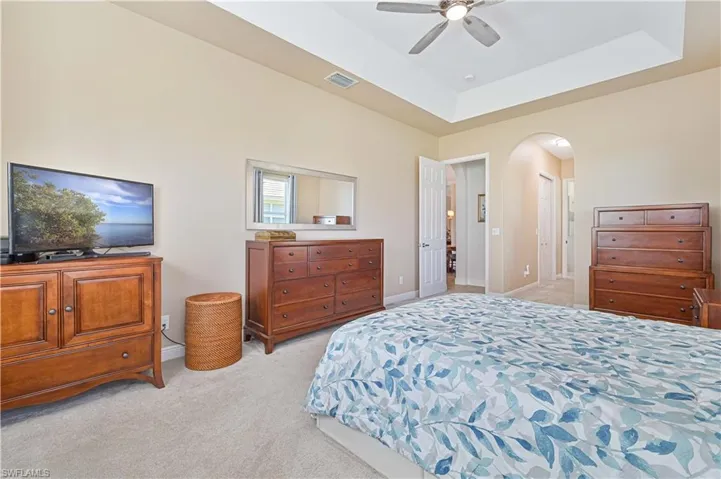 Bedroom featuring light colored carpet, a raised ceiling, and ceiling fan