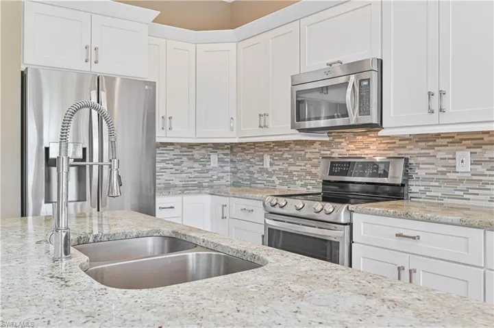 Brand New Kitchen with decorative backsplash, white cabinets, light stone countertops, and appliances with stainless steel finishes