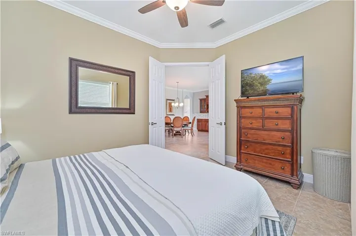 Tiled bedroom with crown molding and ceiling fan with notable chandelier
