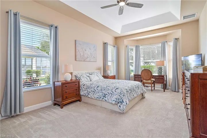 Bedroom featuring a raised ceiling, multiple windows, ceiling fan, and light colored carpet