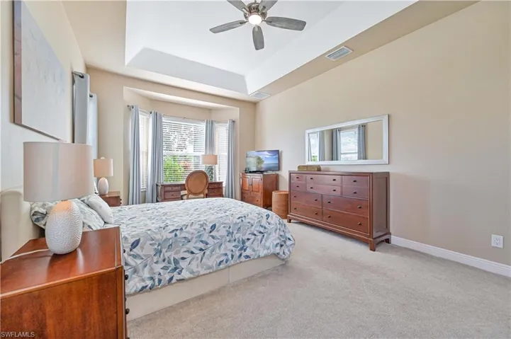Bedroom with ceiling fan, a raised ceiling, and light carpet