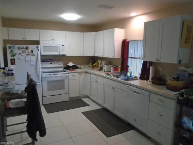 Kitchen with light countertops, visible vents, white appliances, white cabinetry, and a sink