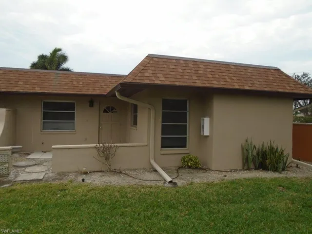 View of front facade featuring a front yard, a shingled roof, and stucco siding