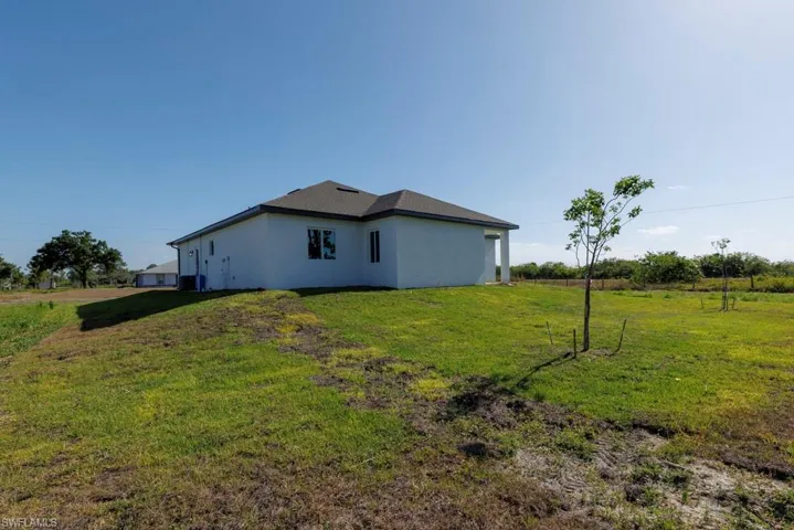 View of side of home with stucco siding, a yard, and central AC