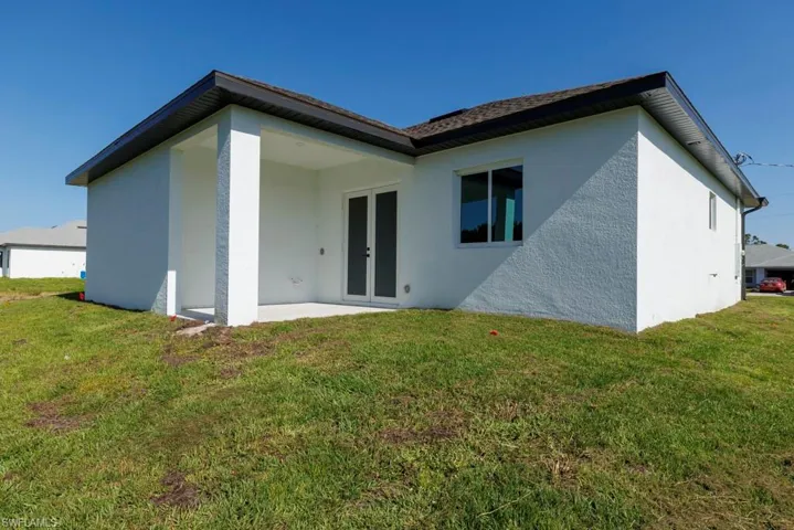 Rear view of property with a lawn, french doors, and stucco siding
