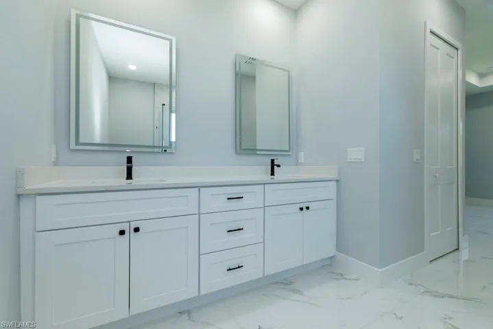 Full bathroom with baseboards, a sink, marble finish floor, and double vanity