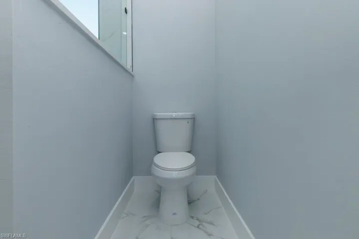 Bathroom featuring baseboards, marble finish floor, and toilet